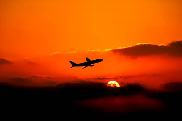 An aircraft climbing above the clouds at sunset